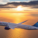 A photo of a United Airlines plane flying over the ocean.